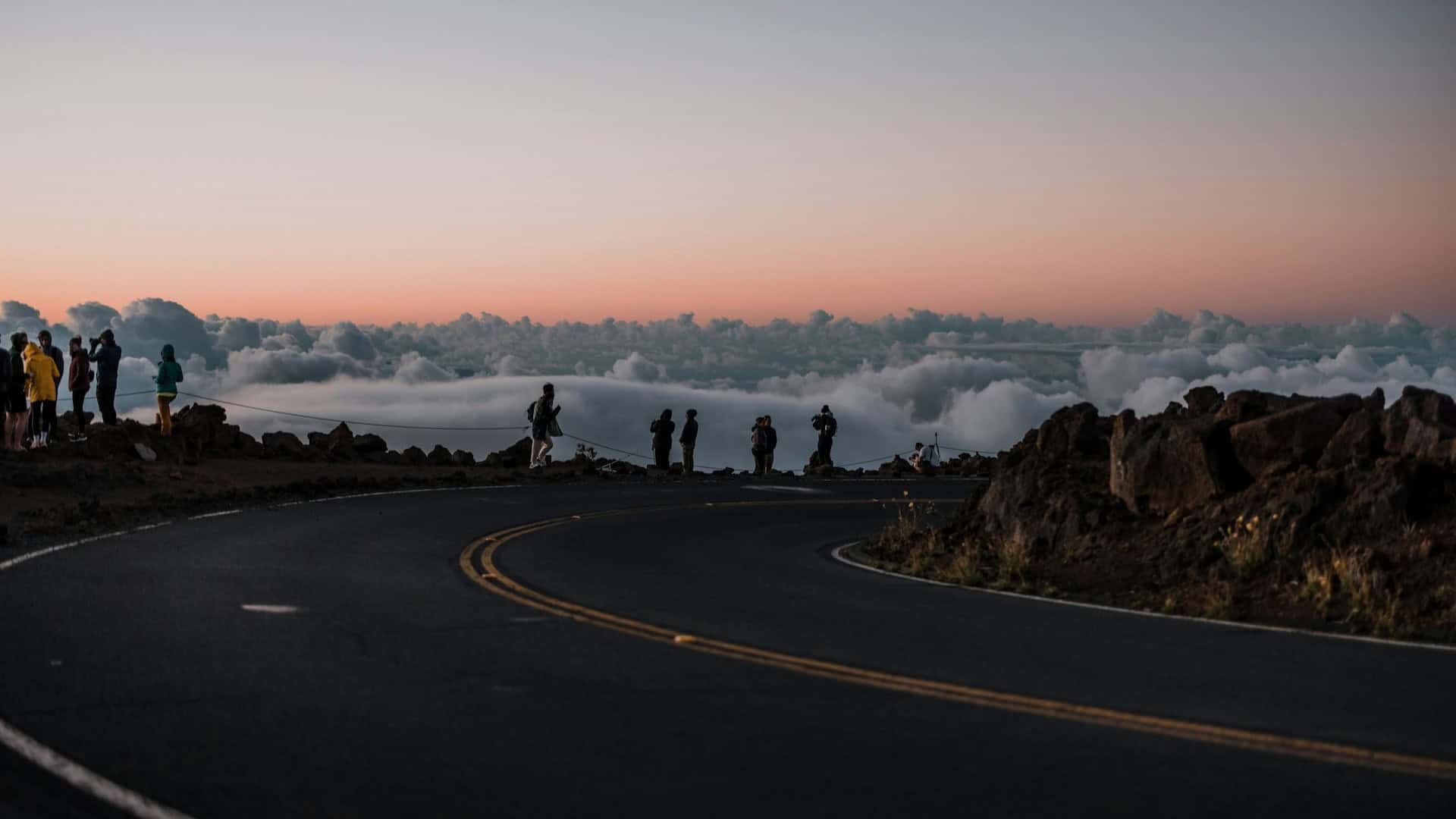 Breathtaking Haleakalā Summit view with people, road, and clouds.
