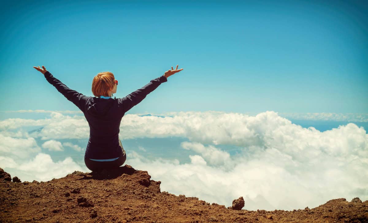 A woman at the summit stretches her arms wide, surrounded by clouds on Maui.