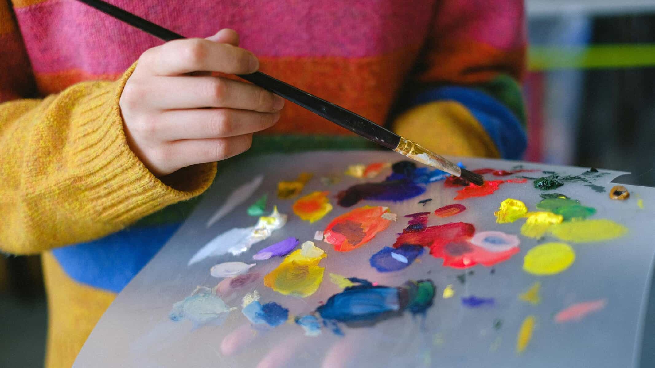 Person holding colorful paints on a paper & brush on a Maui arts workshop.