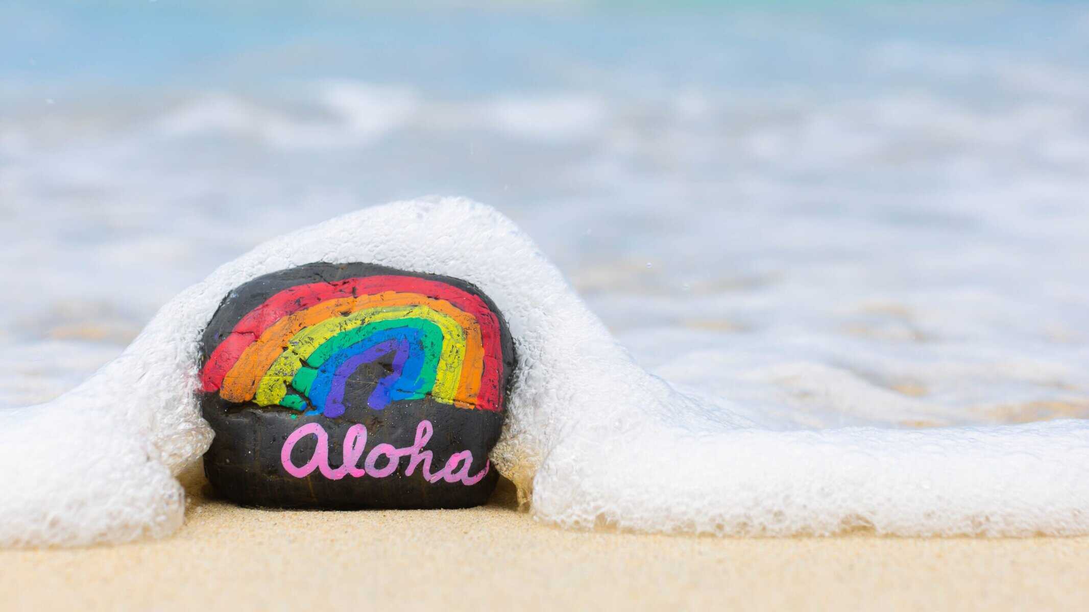 Aloha beach rock on Maui with a vibrant rainbow and ocean waves.