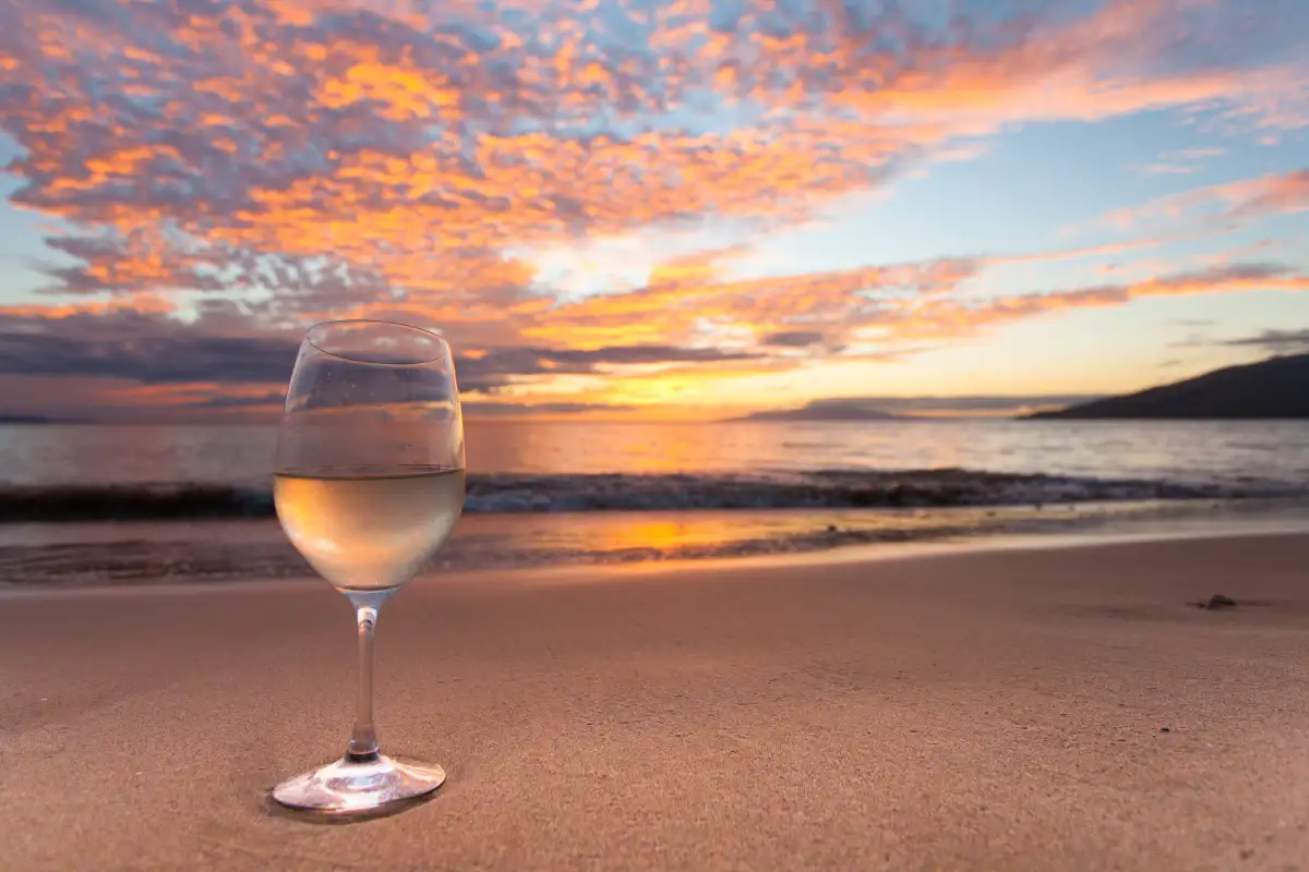 A wine glass on Maui's beach, glowing in the warm sunset light.