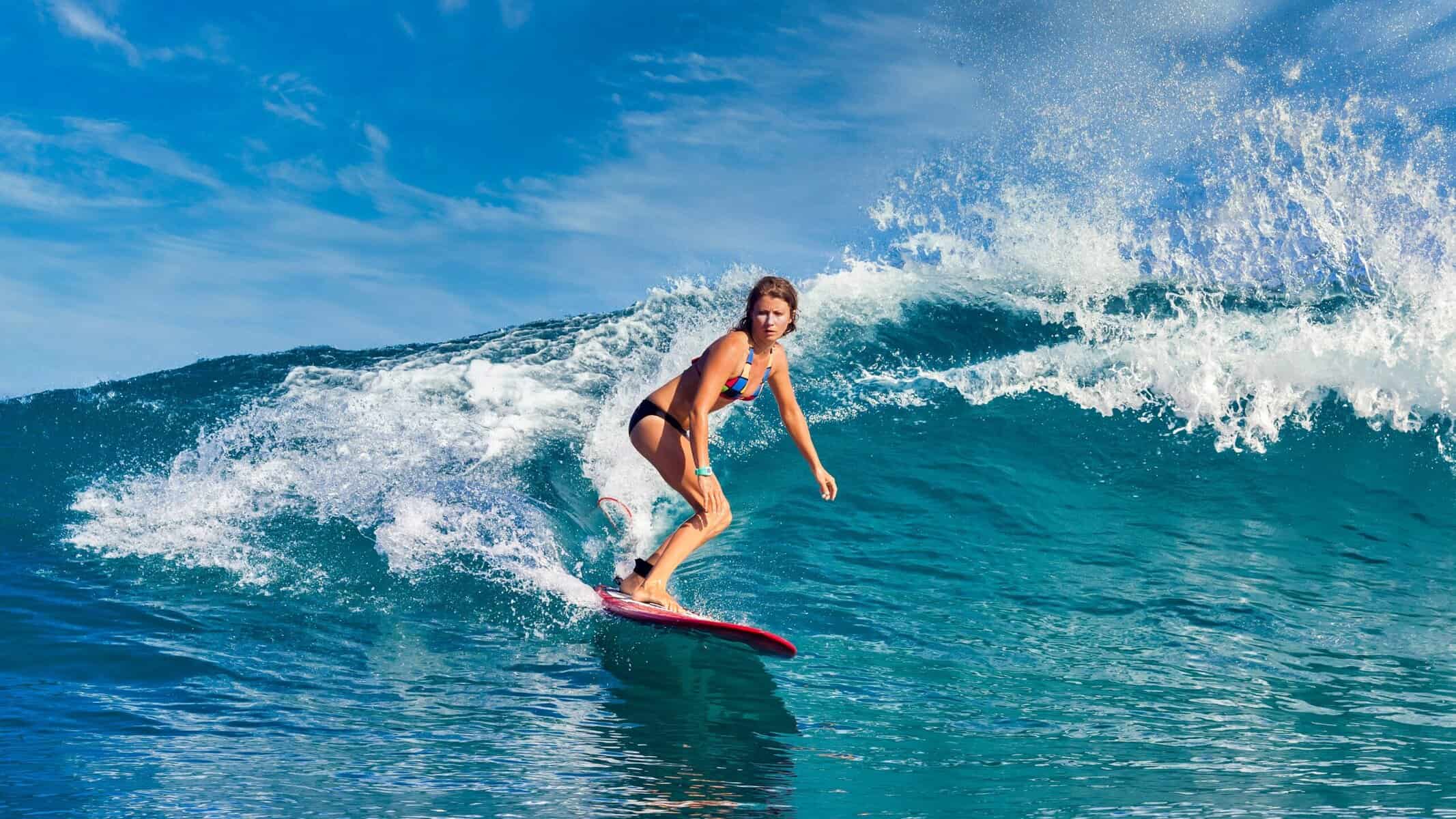 Female surfer riding the blue waves on Maui crystal clear water.
