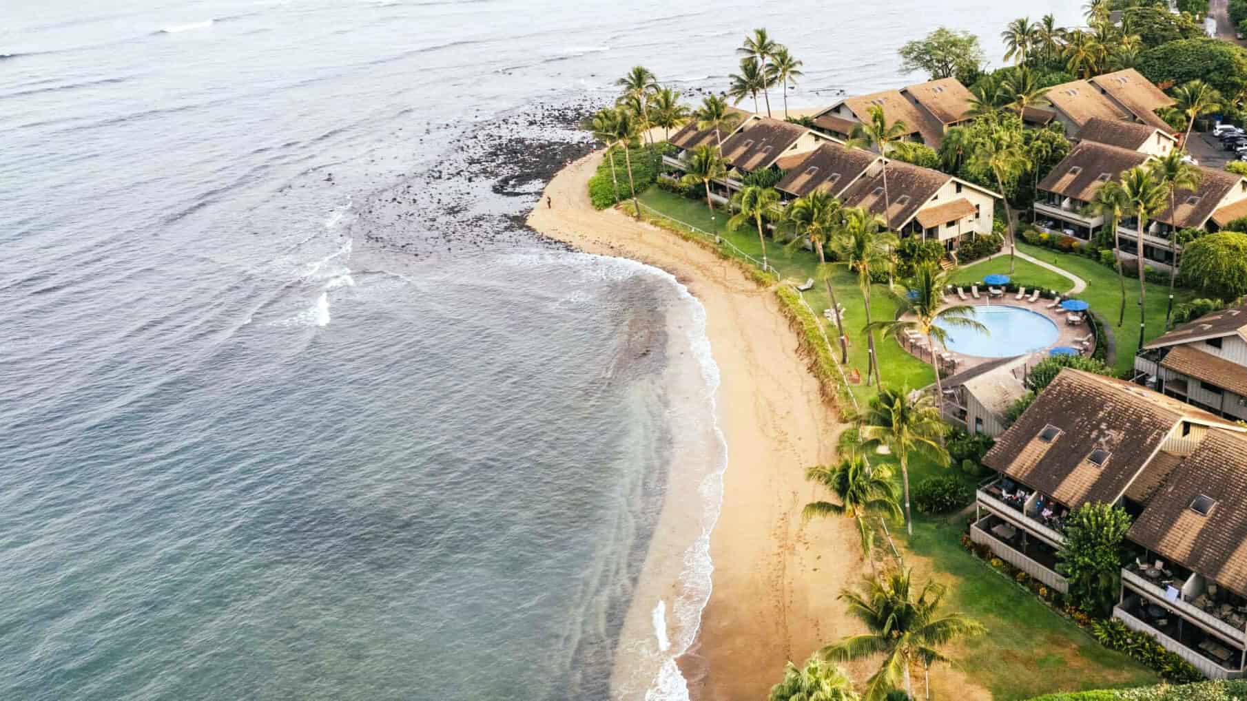 Aerial view of Kahana Village beach resort, highlighting its beachfront and lush greenery.