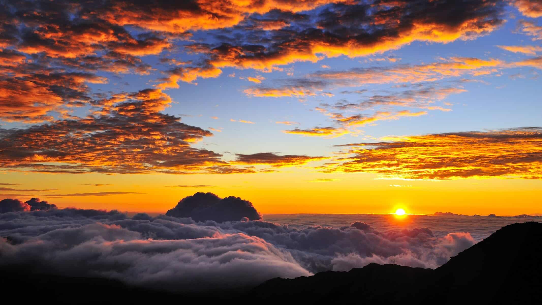 Breathtaking Haleakala sunset over clouds with a majestic mountain silhouette in the background.