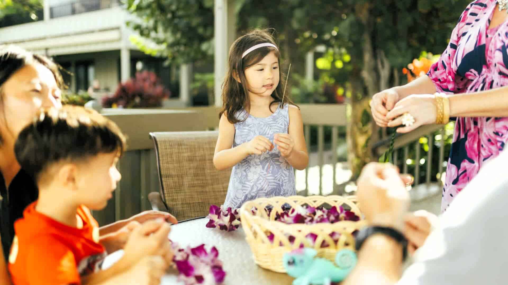 A family enjoys Lei Making at Kahana Village, gathered around a table decorated with vibrant flowers.