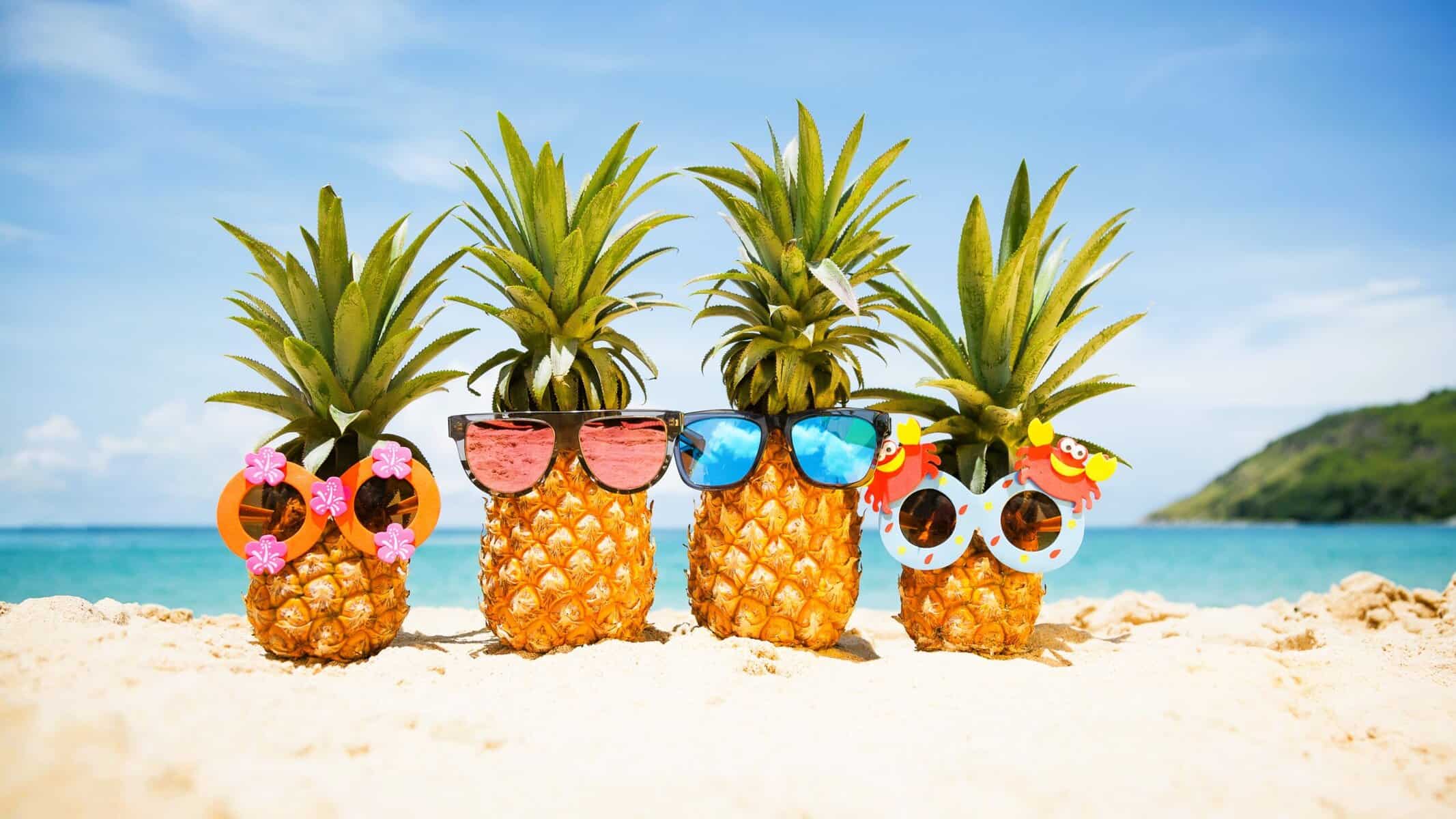 Four cheerful pineapples with sunglasses relaxing on a sunny Maui beach, embodying a playful summer spirit.  