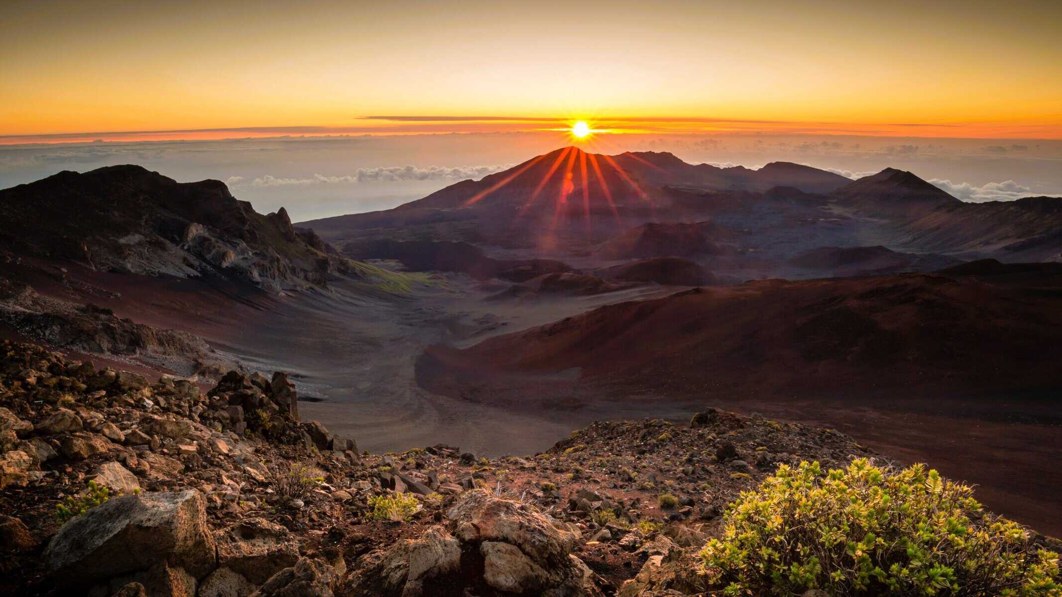 A stunning sunset illuminates the mountains at Haleakala Summit, creating a breathtaking view. 